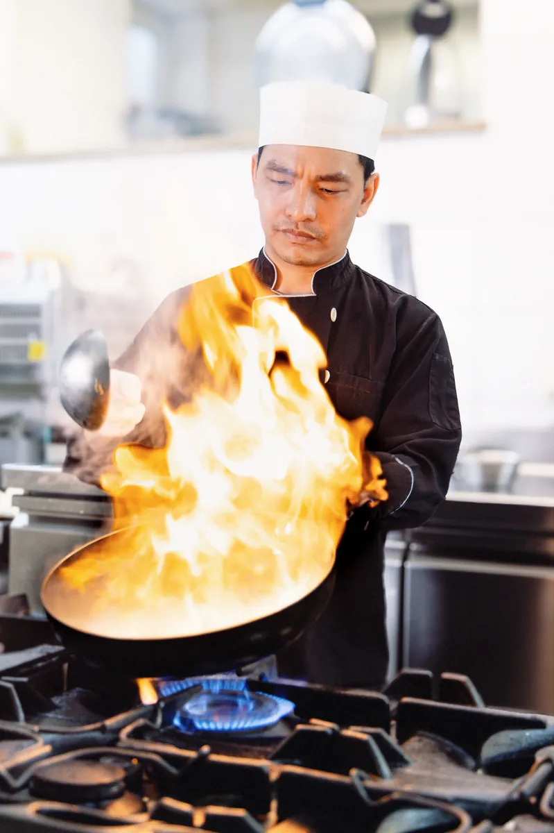 Koch am Wok mit einer hohen Flamme